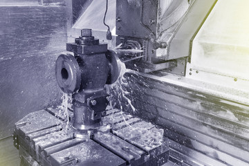 The process of drilling and grinding holes in the body of the valve on the CNC machine. Yellow-green coolant splashes into place