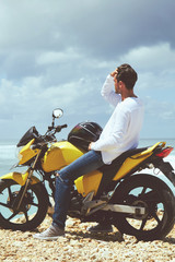 Young handsome man standing near motorcycle on the tropical beach.