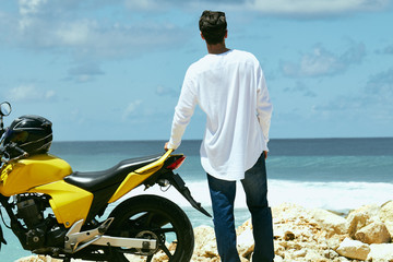Fototapeta premium Young handsome man standing near motorcycle on the tropical beach.