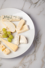 Käseteller mit Edamer, Parmesan, Blauschimmel Käse und Ziegenkäse an Birne und Trauben auf Teller und Marmor Hintergrund