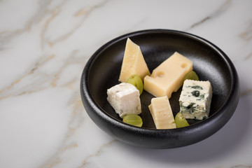 Käseteller mit Edamer, Parmesan, Blauschimmel Käse und Ziegenkäse an Birne und Trauben auf schwarzen Teller und Marmor Hintergrund