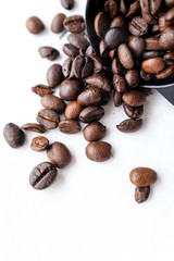 Close up dark roasted coffee beans pouring out of black plastic coffee spoon on white cotton fabric and white filter paper  background in natural light 