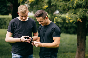 Two young men standing together outdoors looking at photos on a mobile phone