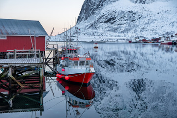 Fishing boat anchored on pier with red village in Lofoten islands