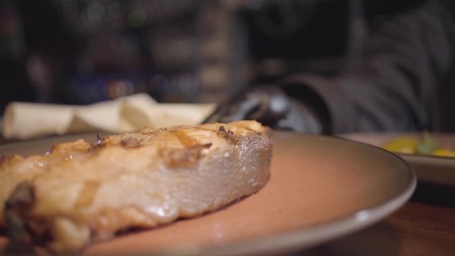 Hand of restaurant chef putting plate with big piece of grilled salmon fish on the table