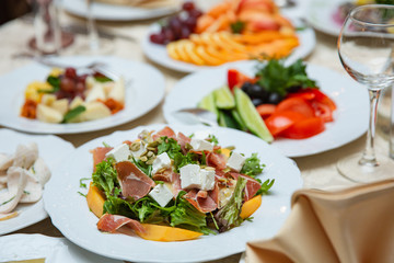 Fresh mix salad with ham, feta and mango on white plate. restaurant table setting
