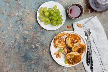 Shrovetide Maslenitsa Butter Week festival meal. Stack of pancakes blini with caramel with nuts, green grape, tea. Russian style, close up top view