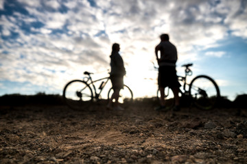 Couple of mountain bikers defocused in background with sunset sky and clouds - focus on the ground - outdoor sport activity for people concept