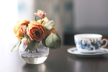 Dry flowers in a glass vase and a cup of tea on a table in an interior.