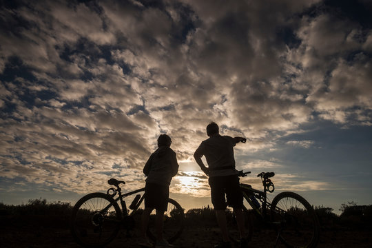 Couple of riders people with mountain bike resting and looking at the dramatic sunset during outdoor sport leisure activity - defocused on the couple and focus on the ground