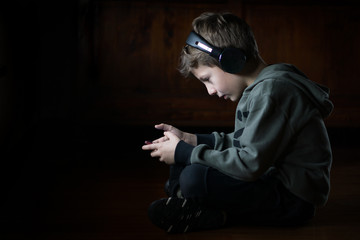 Child playing with a smartphone, wearing headphones and listening music sitting cross-legged