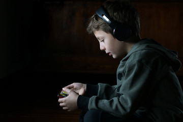 Child playing with a smartphone, wearing headphones and listening music