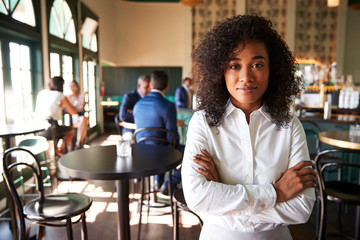 Female Manager Of Busy Cocktail Bar In Restaurant With Customers At Camera