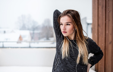 A portrait of young girl or woman with earphones doing stretching outdoors.