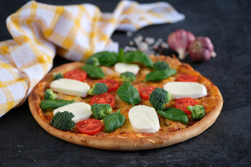 Italian pizza with Mozzarella cheese, tomatoes, broccoli, Spices and fresh basil. Pizza and kitchen napkin near, on black stone background