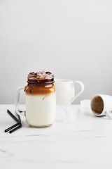 Ice coffee with milk in mason jar and black metal drinking straws on white marble table over white background. Copy space for text.