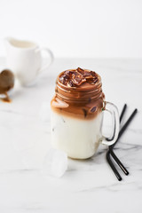 Ice coffee with milk in mason jar and black metal drinking straws on white marble table over white background. Copy space for text.