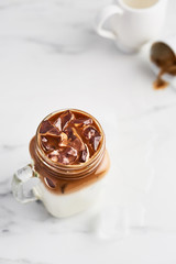 Ice coffee with milk in mason jar on white marble table over white background. Top view. Copy space for text. Selective focus.
