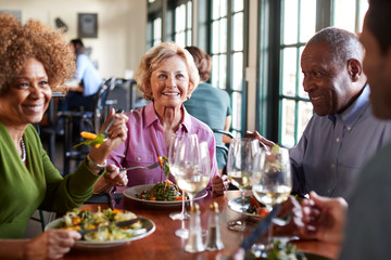 Group Of Smiling Senior Friends Meeting For Meal In Restaurant