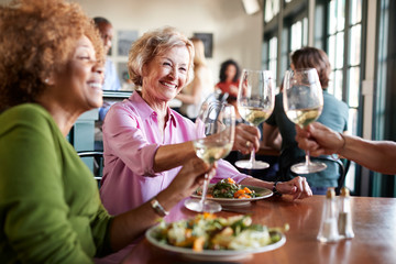 Two Smiling Senior Women Making A Toast At Meal In Restaurant - Powered by Adobe