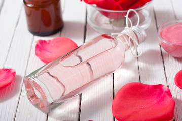 perfume, body care and beauty products with red roses, pink petals on white wood table