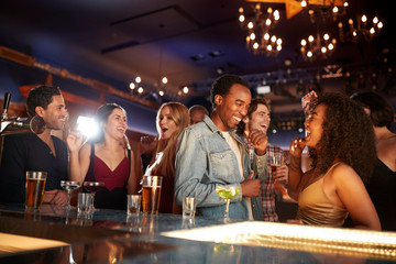 Group Of Couples With Friends Drinking In Bar Together