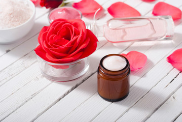 perfume, body care and beauty products with red roses, pink petals on white wood table