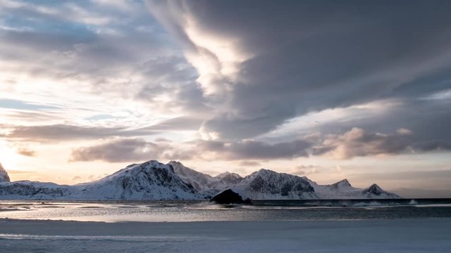 time lapse clouds and islet in Haukland Beach and snow-covered mountains at sunset, Lofoten archipelago, Nordland, Norway