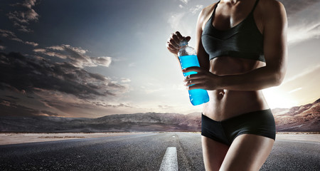 Young girl drinking water of bottle after running, attractive athlete resting after workout outdoors, fitness and healthy lifestyle concept.