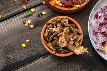 Mixture of vegetables, dried boletus mushrooms, sliced potato, red onion sliced and whole on a cutting board and spices, on old rustic wooden table. With copy space.