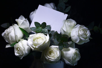 White roses bouquet and greeting card on dark black background. Romantic concept mock up.