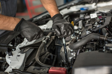 Closeup of strong hands in protective gloves fixing motor of car with wrench in automobile service. Qualified male mechanic in process of repairing broken vehicle. Concept of maintenance.