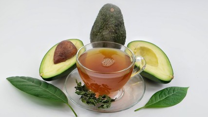 A cup of tea made from avocado leaves and avocado fruits on white background
