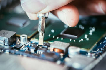 Technician is fixing a computer circuit board, hand and screwdriver.