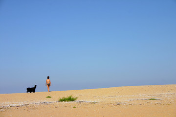 Fototapeta na wymiar Black Sea, Bulgaria. Sunny summer day. Lonely wild beach. Woman in swimsuit and dog look to the sea.