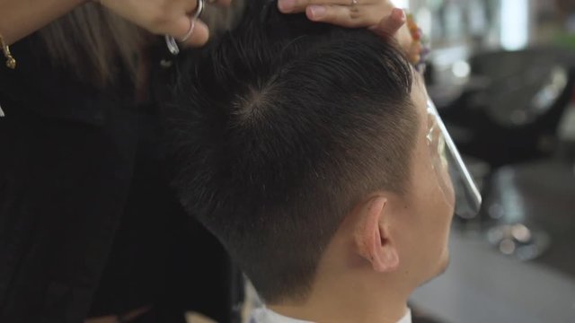 Professional hairdresser cutting customer hair with scissors and comb slow motion.