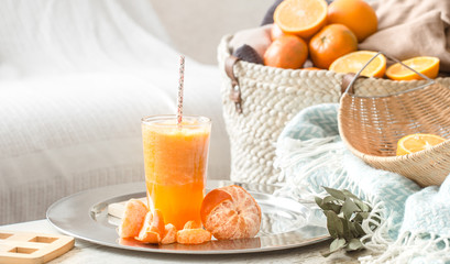 Freshly-grown organic fresh orange juice in the interior of the house, with a turquoise blanket and a basket of fruit