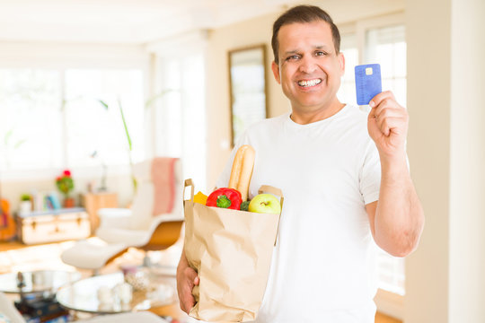 Middle age man holding groceries bag and showing credit card