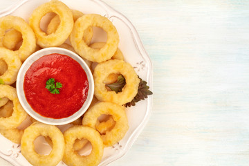 An overhead closeup photo of a plate of squid rings with a red sauce and a place for text