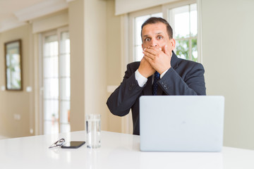 Middle age business man working with computer laptop shocked covering mouth with hands for mistake. Secret concept.