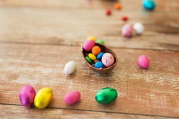 Fototapeta na wymiar easter, sweets and confectionery concept - close up of chocolate egg and candy drops on wooden table