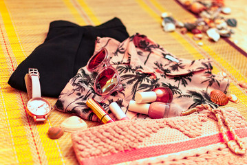 Trendy feminine coral and black outfit flatlay with short, blouse, clutch, sunglasses, watch,  lipgloss and nail polish on straw beach mat. Summer, beach, beauty or fashion blog concept.