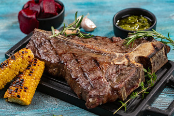 Medium rare grilled Steak Ribeye Black Angus with corn and rosemary on serving board block on blue wooden background