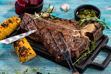 Medium rare grilled Steak Ribeye Black Angus with corn and rosemary on serving board block on blue wooden background