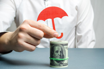 An insurance agent holds a red umbrella over dollar bills. Savings protection. Keeping money safe....