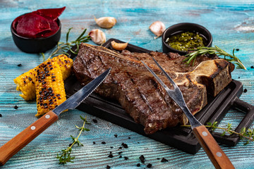 Medium rare grilled Steak Ribeye Black Angus with corn and rosemary on serving board block on blue wooden background