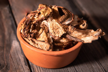 Dried wild boletus mushrooms in vintage ceramic bowl on old wooden table