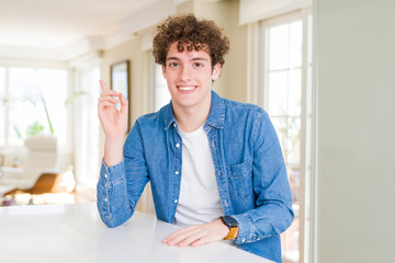 Young handsome man wearing casual denim jacket at home with a big smile on face, pointing with hand and finger to the side looking at the camera.