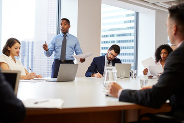 Mature Businessman Standing Giving Presentation To Colleagues In Modern Open Plan Office