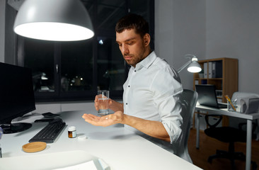 business, overwork and deadline concept - businessman taking medicine pill at night office